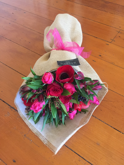 Simply Scarlet - A striking bouquet featuring rich red and vibrant pink shades complemented by fresh greenery. Rustic wrapping and a bright ribbon complete this bold, romantic design.
